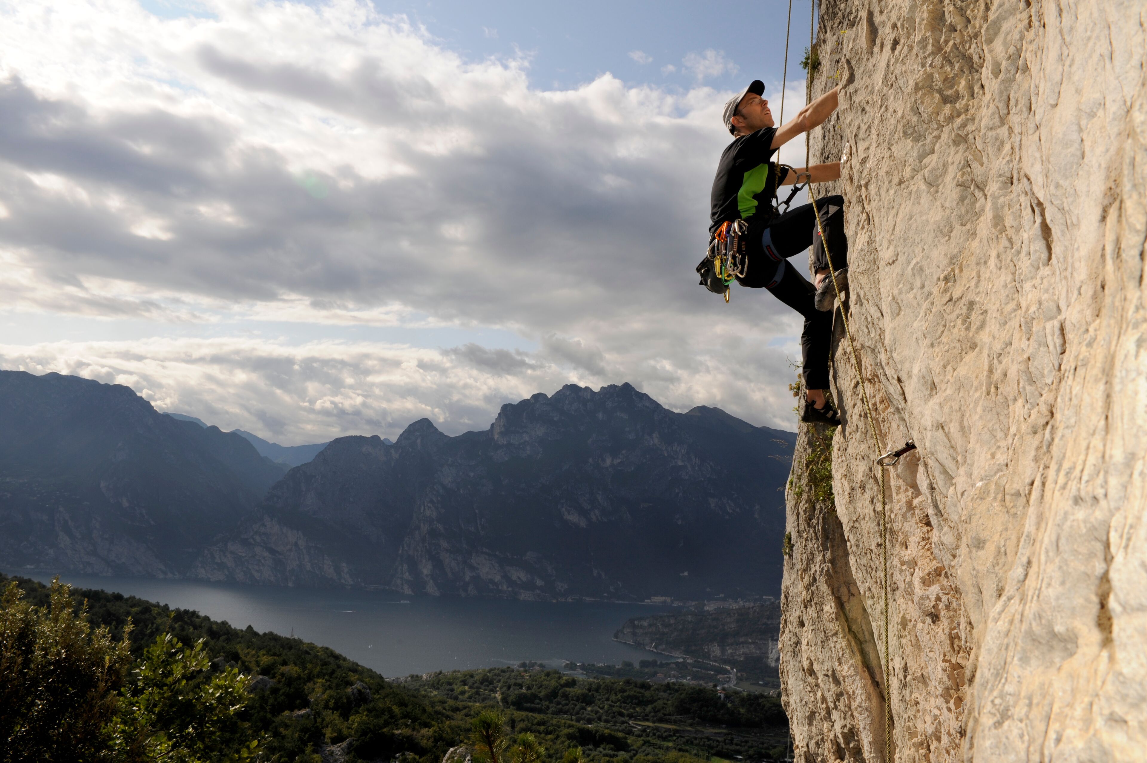 A person rock climbing a steep cliff with a scenic view of mountains and a lake in the background.