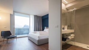 Een moderne hotelkamer met een bed, een stoel, een badkamer met een douchecabine en uitzicht op een berg.