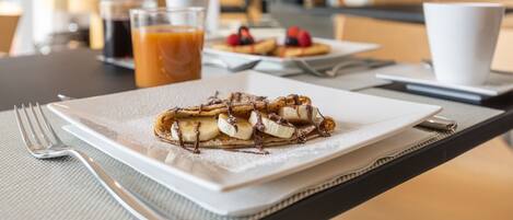 A breakfast setting with a plate of pancakes topped with bananas and chocolate, a cup of coffee, and a glass of orange juice on a table.