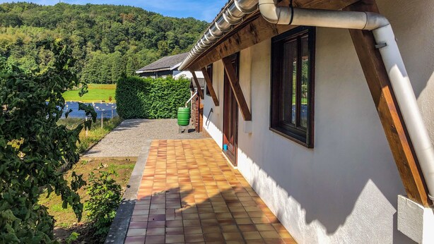 Une maison dotée d’un patio carrelé, d’un balcon en bois et offrant une vue sur un paysage verdoyant et un lac.