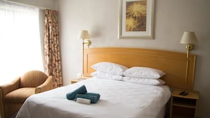 Ein Hotelzimmer mit einem großen Bett, zwei Nachttischlampen, einem Sessel, einem Nachttisch und einem gerahmten Bild an der Wand.