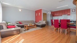 A modern living room with a sofa set, a coffee table, and a dining area with red chairs. - Village House Imotski (Imotski)