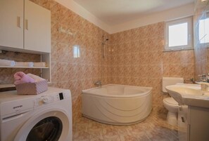 A bathroom with a washing machine, a bathtub, and a toilet.