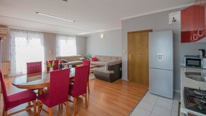 A modern apartment with a dining area, a living room with a sofa, a kitchen with a refrigerator and microwave, and a wooden door. - Village House Imotski (Imotski)