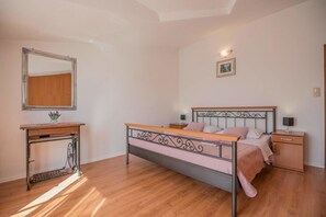 A bedroom with a metal-framed bed, a wooden desk, a mirror, and a nightstand.