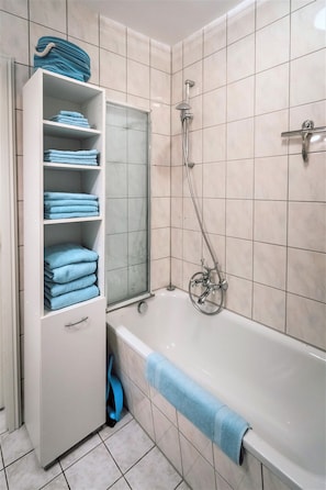 A bathroom with a white bathtub, a glass shower enclosure, and a built-in shelf with folded towels.