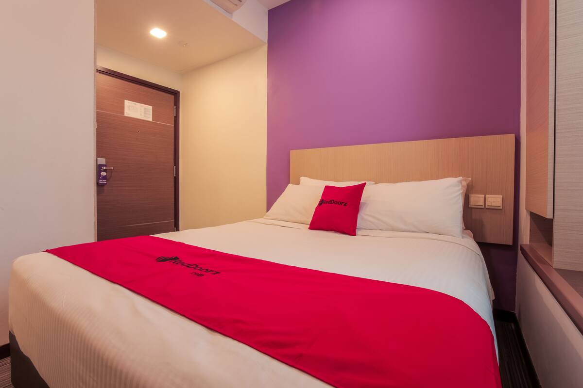Una habitación de hotel con una cama, una manta roja y una pared morada.