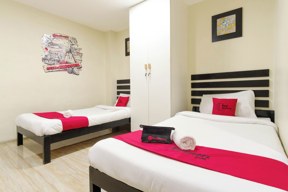 A hotel room with two beds, a red towel, a RedDoorz bag, and a wall poster.