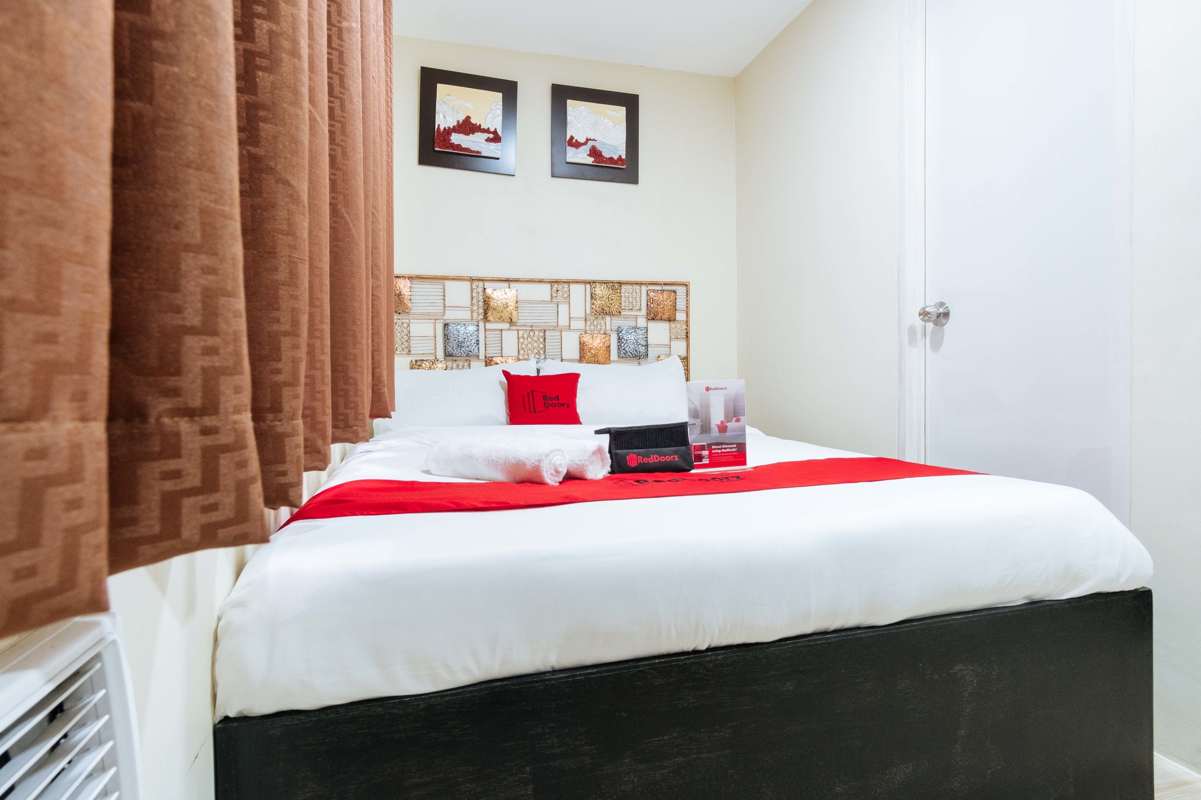 A neatly made bed with a white and red bedspread, a black headboard, and a red pillow. There are two framed pictures on the wall above the bed.
