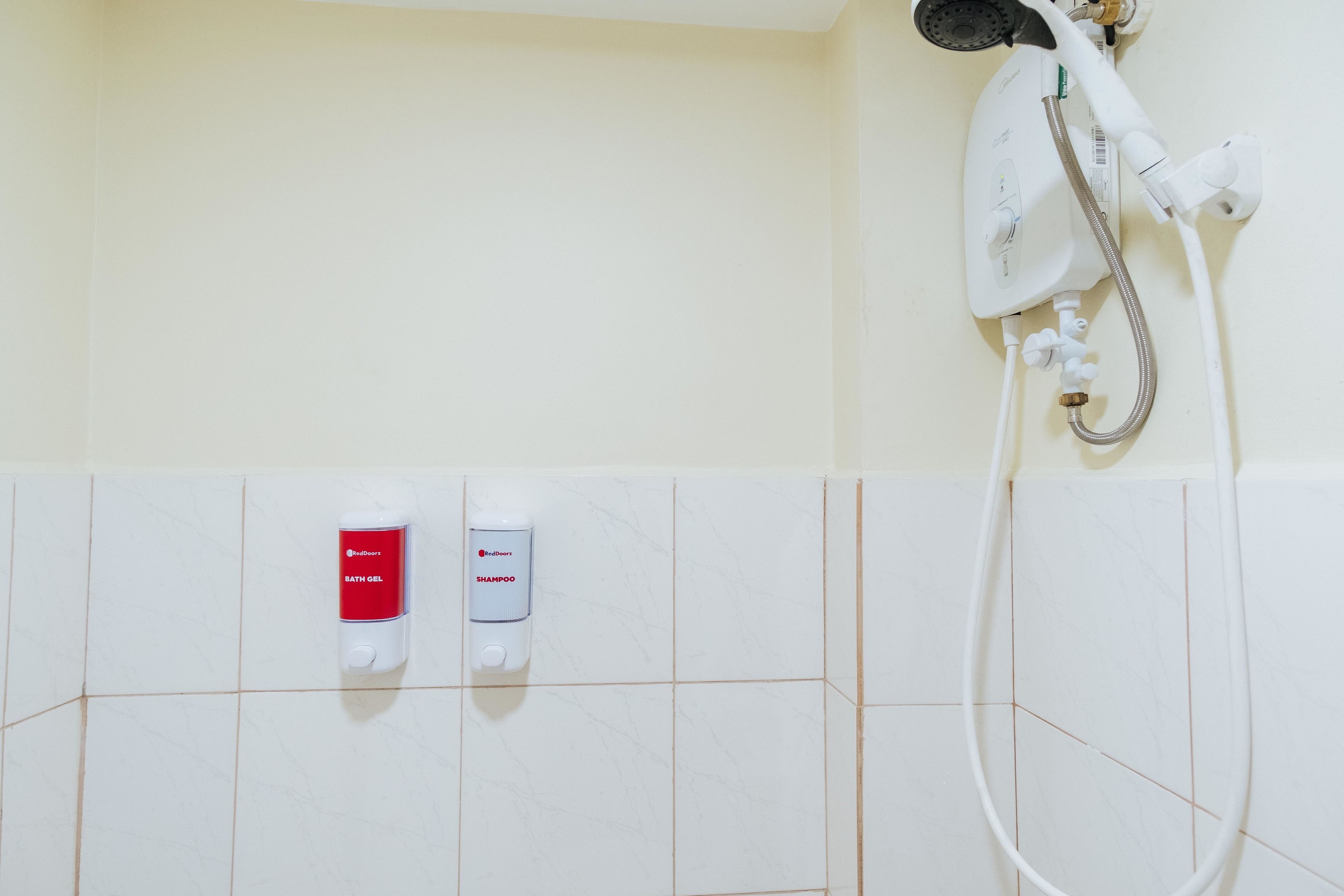 A bathroom with a shower, a hand dryer, and two dispensers for bath gel and shampoo.