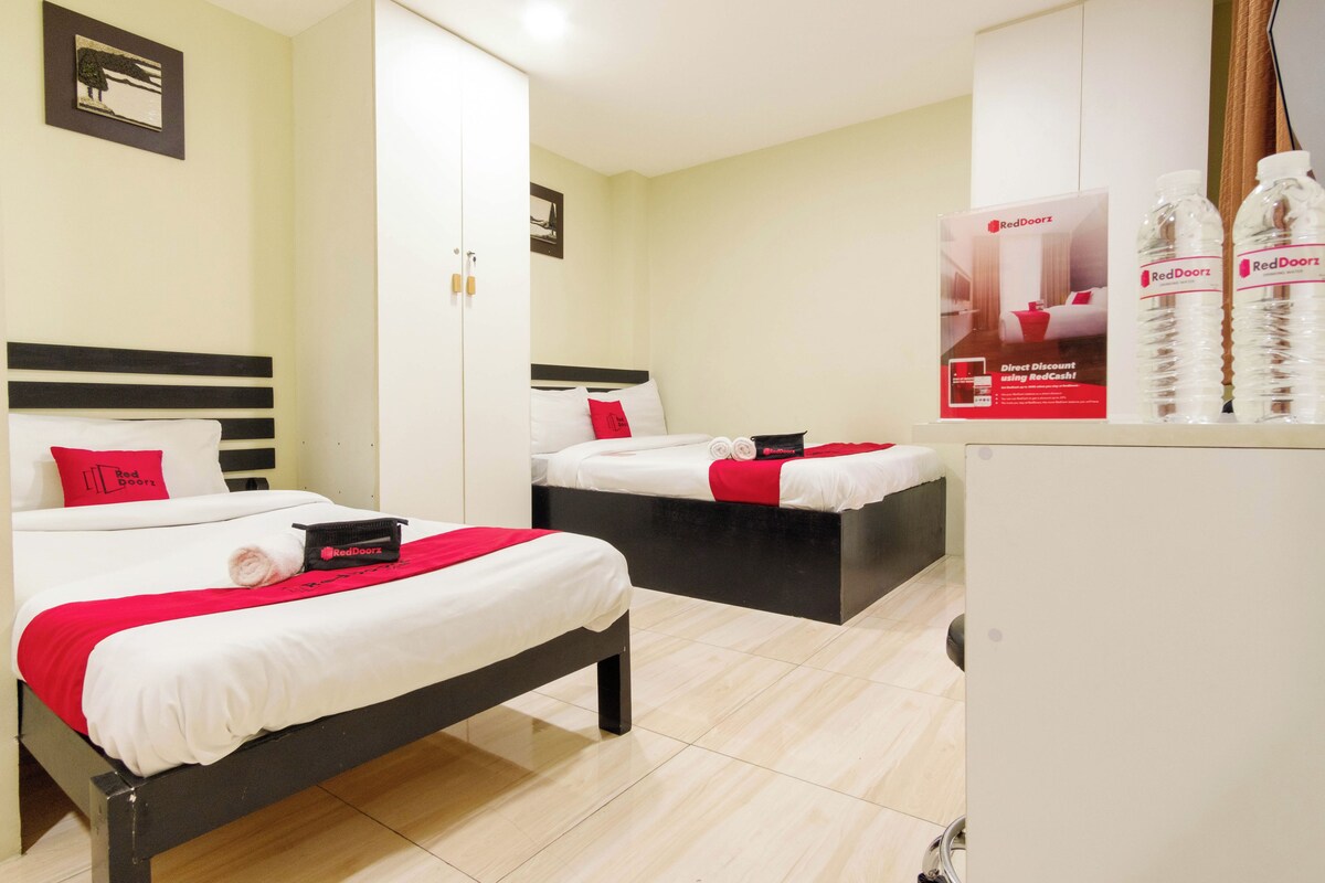 A hotel room with two beds, a wardrobe, a refrigerator, and RedDoorz water bottles.