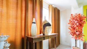 Una habitación con una consola de madera, dos jarrones decorativos, una planta en maceta y una ventana con cortinas.