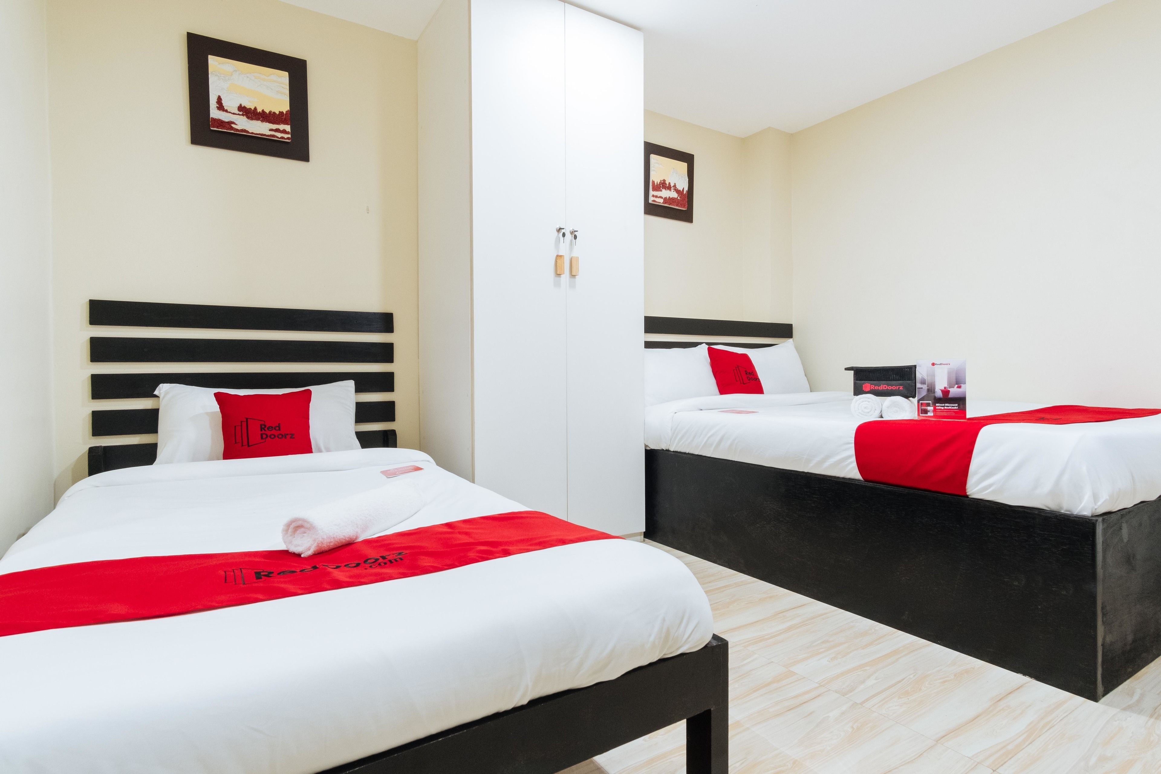 A hotel room with two beds, each with white bedding and red accents, a black headboard, and a red towel on the bed.