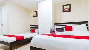 Habitación de hotel con dos camas, cada una con ropa de cama blanca y detalles rojos, un armario blanco y un cuadro en la pared.