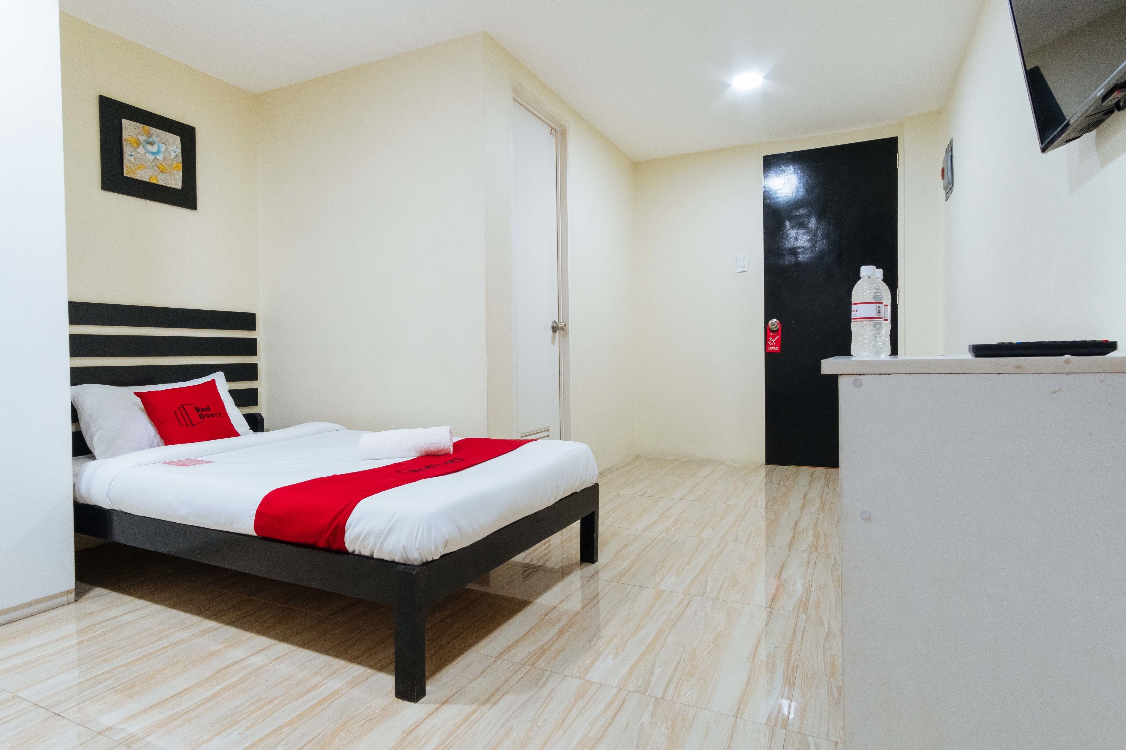 A hotel room with a bed, a desk, a chair, a door, and a wall-mounted TV.