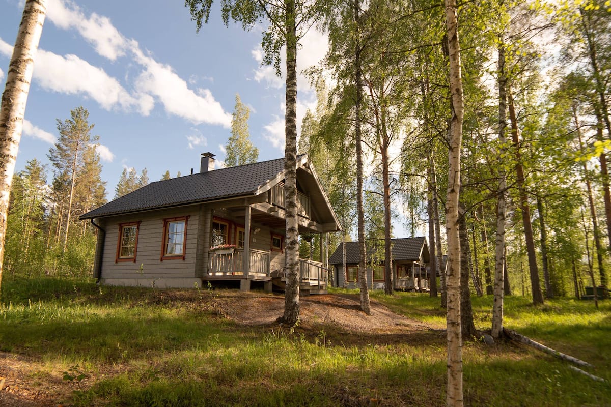 A cabin with a porch, surrounded by tall trees and a clear sky.