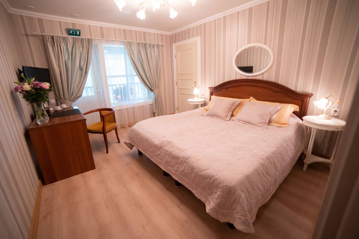 A neatly arranged bedroom with a large bed, bedside tables, a chair, and a window with curtains.