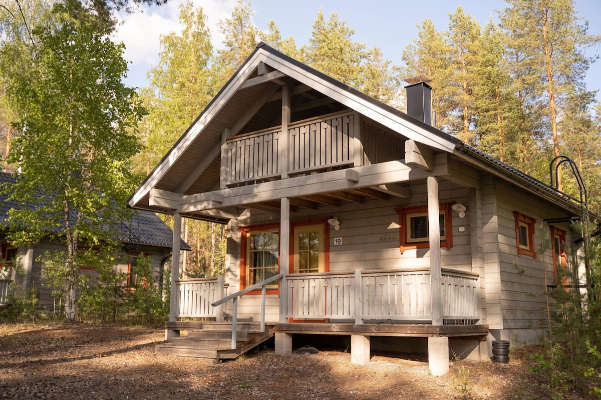 A wooden cabin with a balcony, a front porch, and a chimney.
