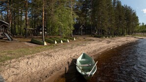 Ein Sandstrand mit einer Reihe grüner Kanus, ein kleines Boot im Wasser und eine Hütte im Hintergrund.