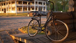 Ein Fahrrad auf einer Holzterrasse, im Hintergrund eine große Blockhütte.