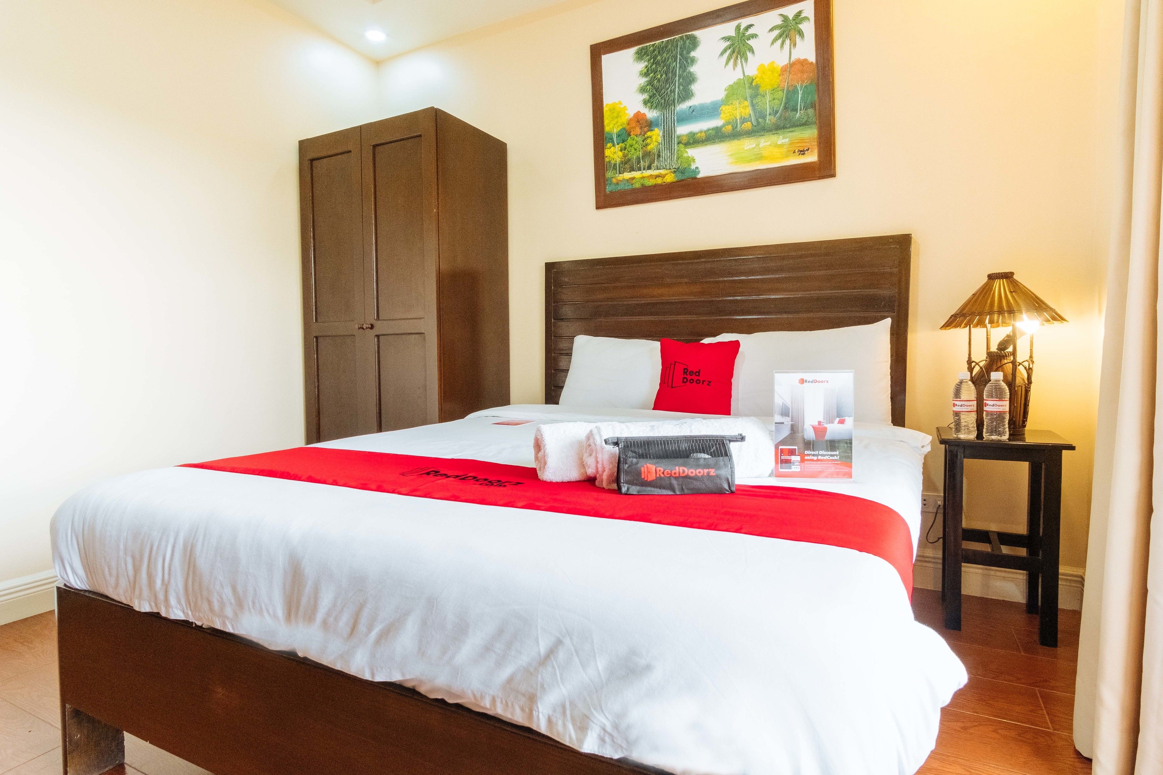 Una cama bien hecha con una colcha roja y blanca, un cabecero de madera y un cuadro de un paisaje en la pared.