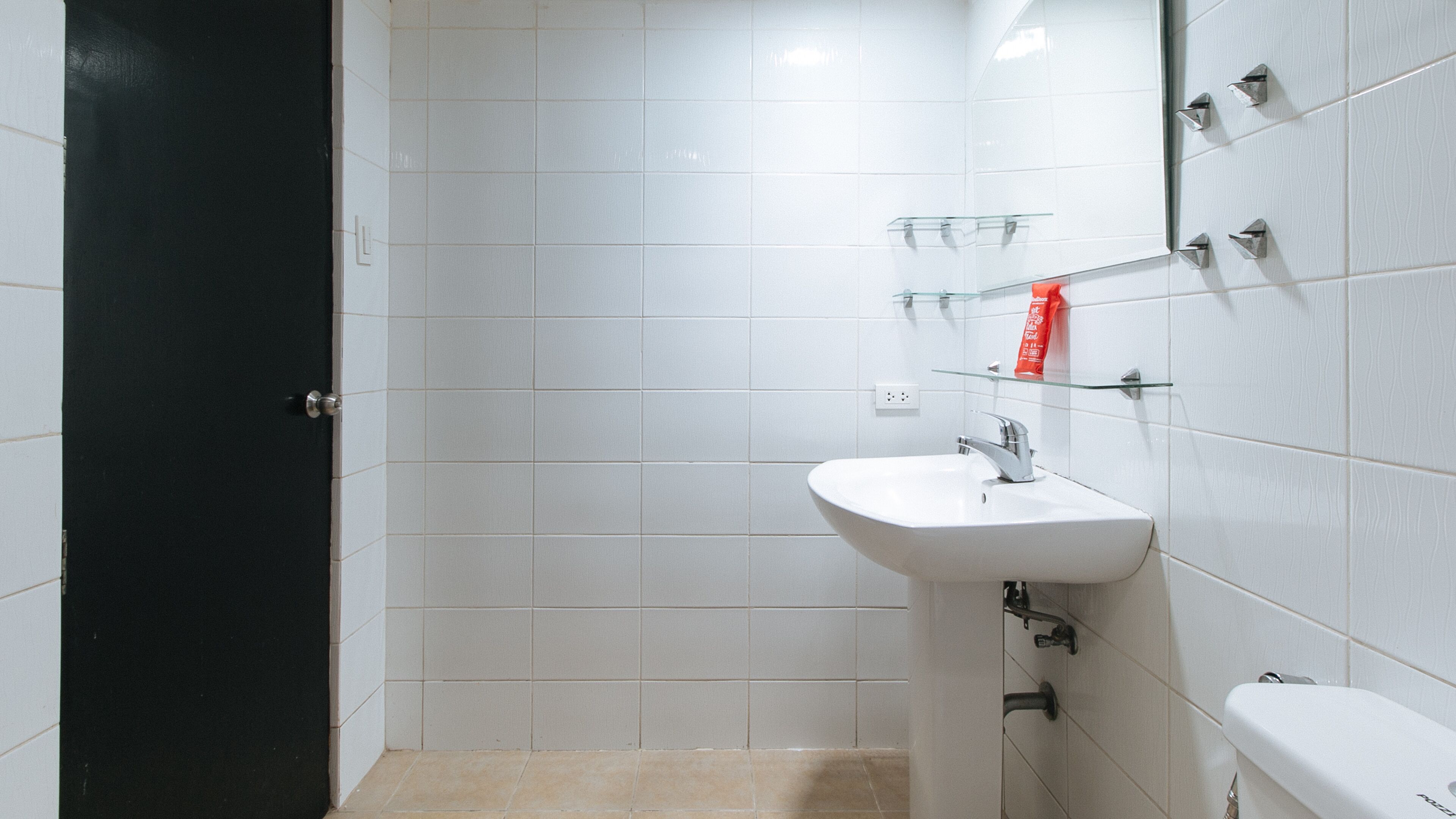 Une salle de bain avec des carreaux blancs, un lavabo blanc, un miroir et une porte noire.
