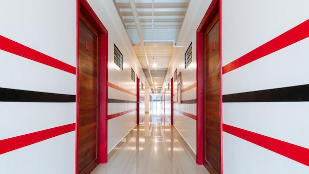 A long, narrow hallway with red and white walls, wooden doors, and a shiny floor. - RedDoorz Plus near UST Manila (Manila)