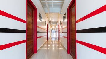 A long, narrow hallway with red and white walls, wooden doors, and a shiny floor.