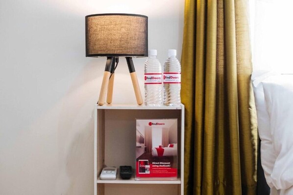 A hotel room with a bedside table holding a lamp, two RedDoorz water bottles, a scale, and a RedDoorz promotional box. - RedDoorz @ San Antonio Binan (Biñan City)