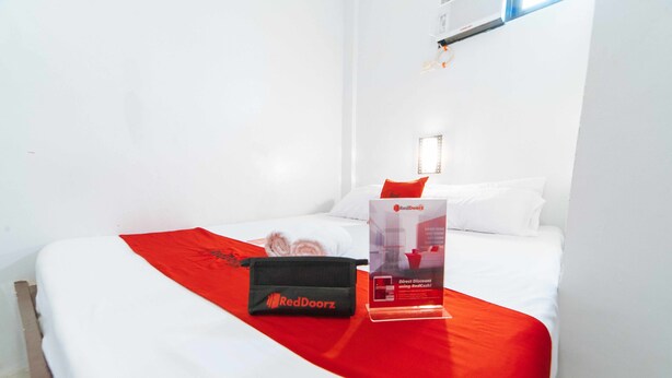 Une chambre d’hôtel avec un lit soigneusement fait, un plaid rouge, un sac RedDoorz et un présentoir promotionnel.