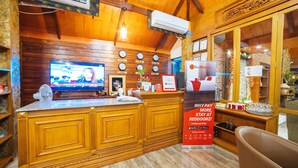 A wooden reception desk with a television, clocks, and a sign promoting a service. - RedDoorz Plus @ Starhomes Olivianville (Tarlac)