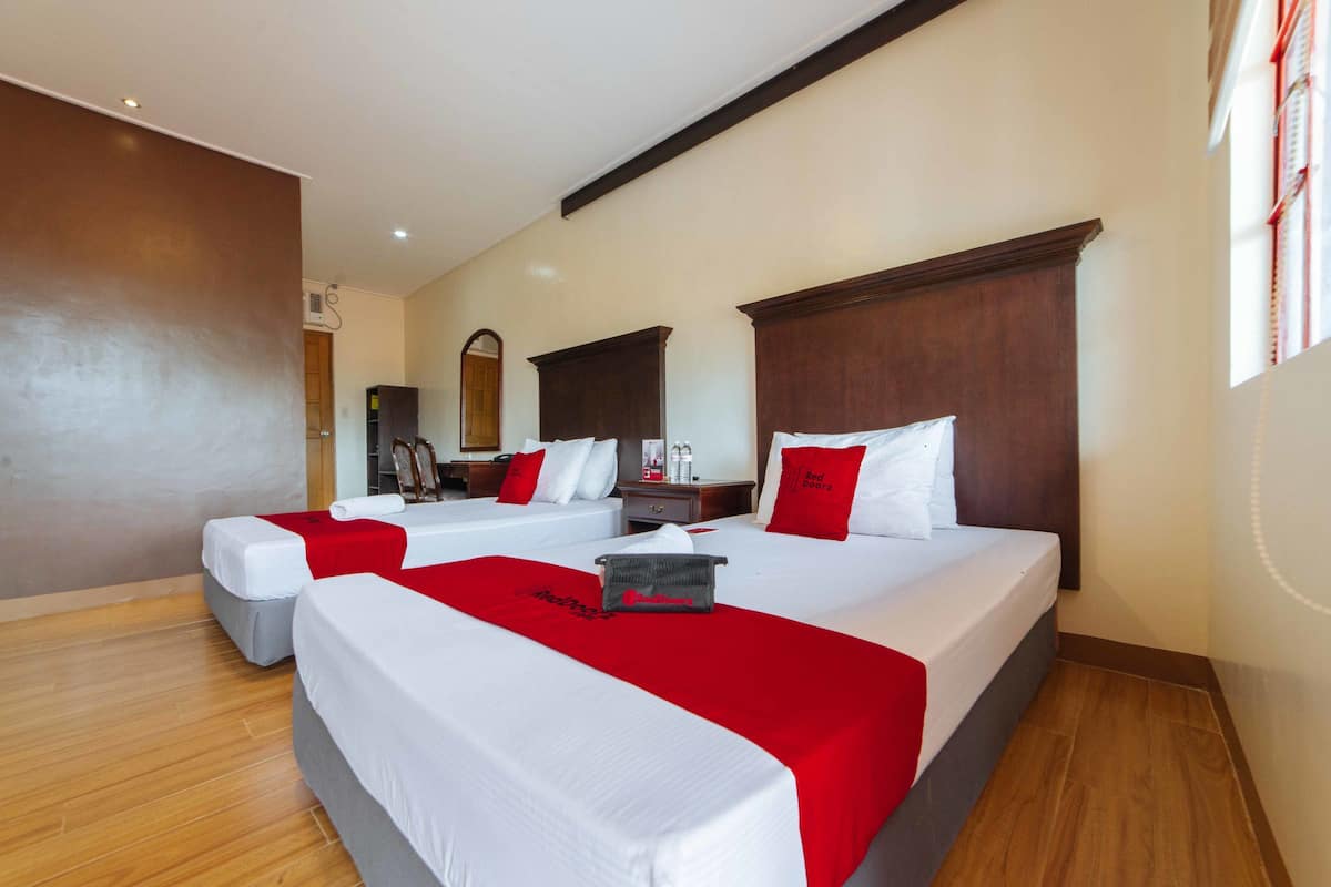 Ein Hotelzimmer mit zwei Betten, einem hölzernen Kopfteil und einem roten Zierkissen.