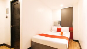Une chambre d’hôtel avec un lit, une porte sombre, un climatiseur fixé au mur et un oreiller rouge.