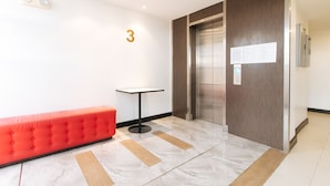 Un hall d’entrée moderne avec un banc rouge, une petite table et un ascenseur.