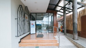 L’entrée d’un hôtel, avec une porte en verre, des marches en bois, une rampe métallique et une clôture en bambou.