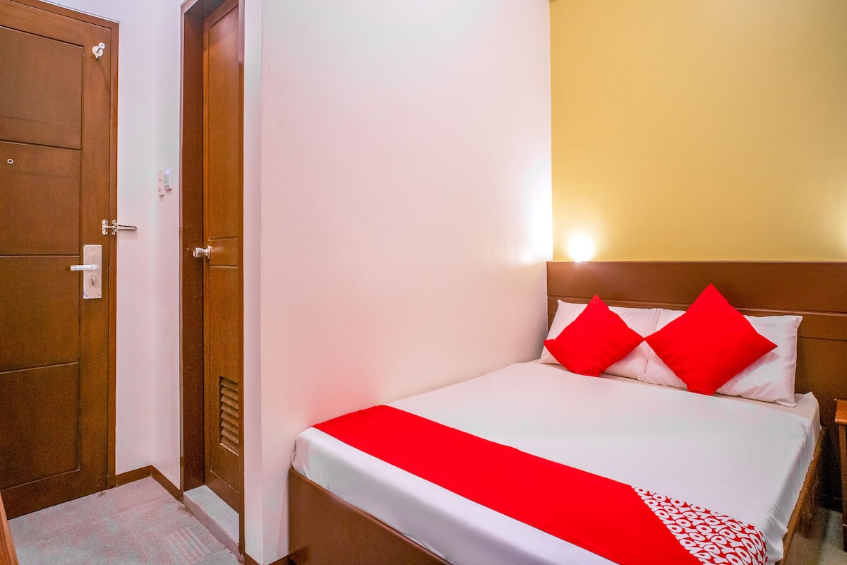 A hotel room with a bed, a wooden door, and a wall-mounted light fixture.