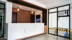 Una recepción con diseño moderno, que presenta una superficie blanca y detalles de madera. Hay tres lámparas colgantes sobre el mostrador y un televisor de pantalla plana montado en la pared.