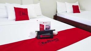 A hotel room with two beds, each with white bedding and red pillows. A red towel and a RedDoorz promotional bag are placed on the bed. - RedDoorz @ VP Inting Street (Tagbilaran)
