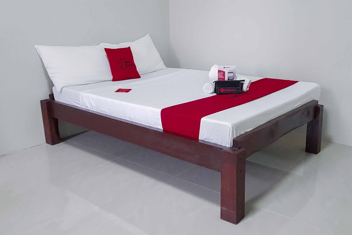 A bed with white bedding, a red accent pillow, and a red throw blanket.