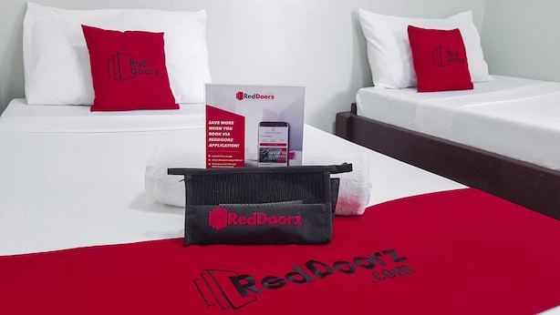 A hotel room with two beds, each with a white mattress and red pillows. There is a RedDoorz promotional stand and a RedDoorz branded bag on the bed. - RedDoorz @ VP Inting Street (Tagbilaran)
