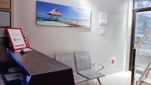 A reception area with a wooden desk, a framed sign, a beach-themed painting, and a glass door leading outside. - RedDoorz @ VP Inting Street (Tagbilaran)