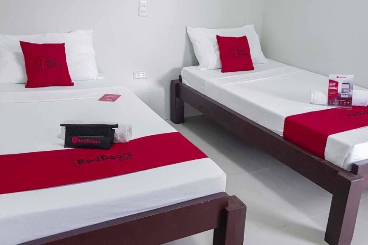 Two single beds with white linens and red accents, a red blanket, and a RedDoorz branded item on the left bed.