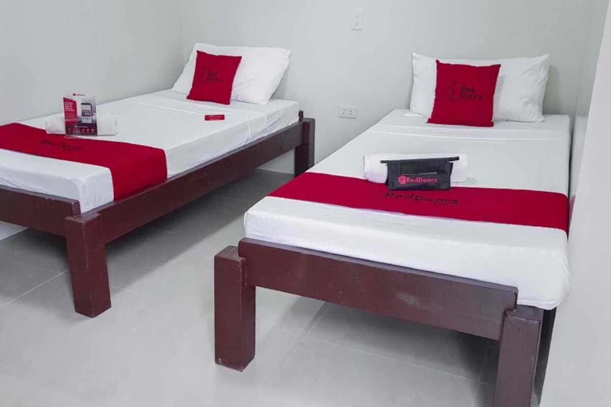 Two single beds with wooden frames and white bedding, each with a red pillow and a red blanket.