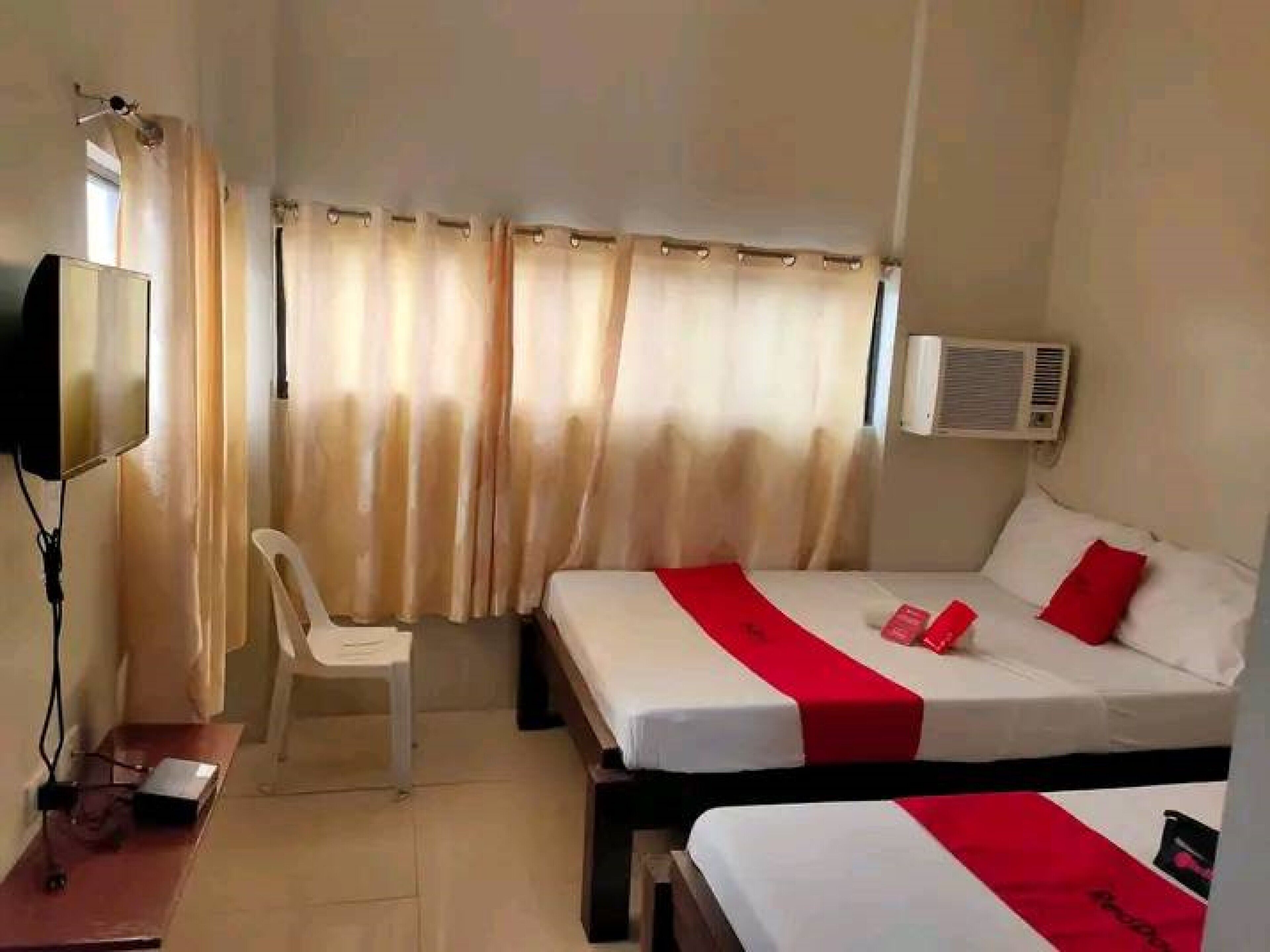 Quarto de hotel com duas camas, uma escrivaninha, uma cadeira, uma televisão e um aparelho de ar condicionado.