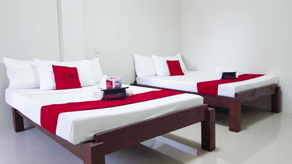 Duas camas de solteiro com roupa de cama branca e detalhes vermelhos, cabeceiras de madeira e um cobertor vermelho em cada cama.