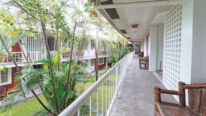 A corridor with a balcony, white railings, and a view of a garden with palm trees. - RedDoorz Premium @ Clarkview Angeles City (Angeles City)