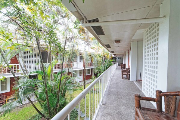A corridor with a balcony, white railings, and a view of a garden with palm trees. - RedDoorz Premium @ Clarkview Angeles City (Angeles City)