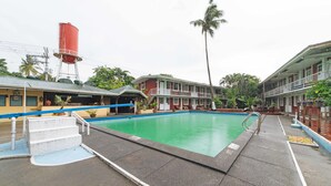 A swimming pool with a concrete deck, a red water tower, and a two-story building with balconies. - RedDoorz Premium @ Clarkview Angeles City (Angeles City)