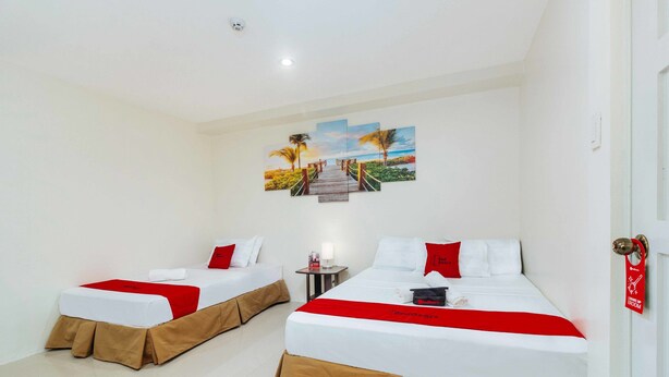 A hotel room with two beds, each with a red and white bedspread, and a painting of a beach scene on the wall. - RedDoorz @ Salinas Extension Lahug (Cebu City)