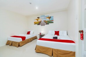 Una habitación de hotel con dos camas, cada una con una colcha roja y blanca, y un cuadro con una playa en la pared.